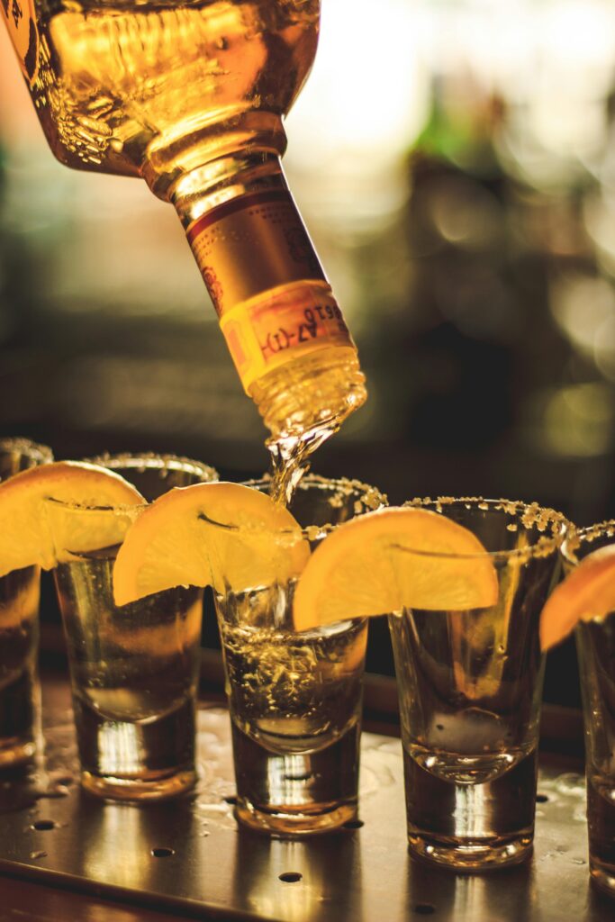 Bartender pouring alcohol into shot glasses garnished with lemon slices, perfect for nightlife imagery.